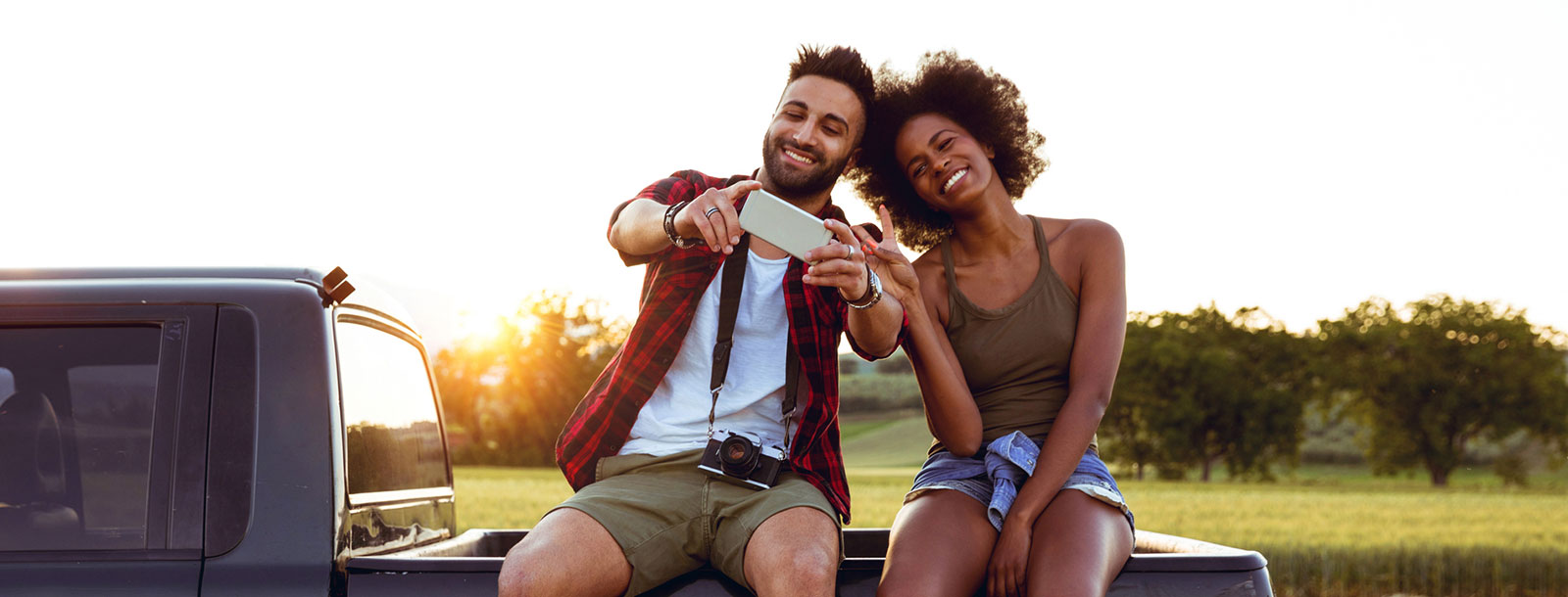 Young couple sitting on back on truck taking selfie.